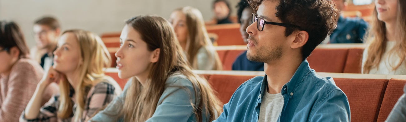 Mehrere Studierende sitzen in einem Hörsaal und hören einem Dozenten zu. 